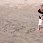 Oskar skriver sitt namn i sanden