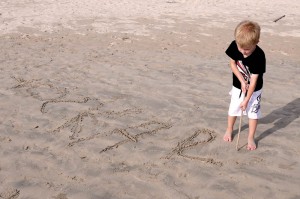 Oskar skriver sitt namn i sanden